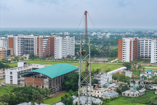 Trishal Upazila Bangladesh 13 May 2026 Aerial view of workers climbing a tall metal tower on a university campus with modern buildings and green landscapes. Trishal Upazila Bangladesh 13 May 2026 Aerial view of workers climbing a tall metal tower on a university campus with modern buildings and green landscapes.