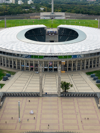 Berlin Germany 26 September 2026 Aerial view of Olympiastadion Berlin showing the iconic stadium architecture circular roof paved forecourt with people and surrounding parkland.