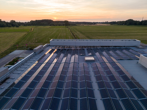 Aerial view of solar panels installed on a large industrial roof during a golden sunset with surrounding green fields and rural landscape in Zemst Flanders Belgium. Aerial view of solar panels installed on a large industrial roof during a golden sunset with surrounding green fields and rural landscape in Zemst Flanders Belgium.