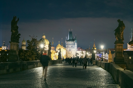 Prague Czechia 03 November 2021 View of Charles Bridge at night with pedestrians on the cobblestone path illuminated statues and the Old Town Bridge Tower under a dark sky. Prague Czechia 03 November 2021 View of Charles Bridge at night with pedestrians on the cobblestone path illuminated statues and the Old Town Bridge Tower under a dark sky.