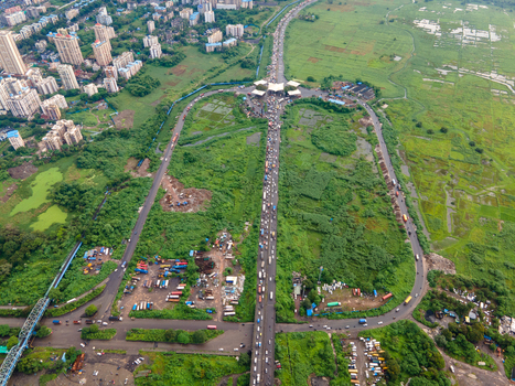 Aerial view of a busy highway junction in Thane surrounded by lush green fields industrial areas and residential high rise buildings in the distance Thane Maharashtra India. Aerial view of a busy highway junction in Thane surrounded by lush green fields industrial areas and residential high rise buildings in the distance Thane Maharashtra India.