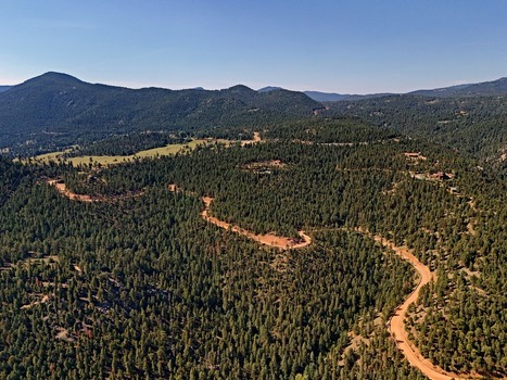 Aerial view of the winding dirt road leading to Crescent Meadows Trailhead surrounded by dense pine forests and rolling mountain terrain in Golden Colorado United States. Aerial view of the winding dirt road leading to Crescent Meadows Trailhead surrounded by dense pine forests and rolling mountain terrain in Golden Colorado United States.