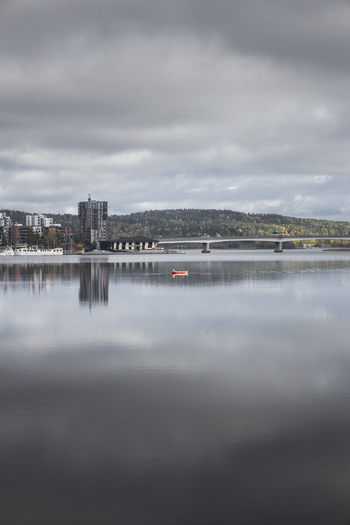 View of the calm waters of Lake Jyvasjarvi with a small red boat the city skyline and a bridge under a cloudy sky in Jyvaskyla Central Finland Finland.