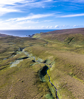 Aerial view of the rugged landscape of An Port featuring a winding stream cutting through green and brown hills leading towards the Atlantic Ocean in Ardara County Donegal Ireland.