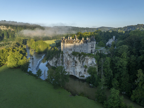 Aerial view of Chateau de Walzin perched on a cliff above the Lesse river surrounded by lush forest and morning mist in Dinant Region wallonne Belgium.