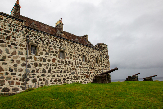 View of Duart Castle featuring historic stone walls and ancient cannons on a grassy hill under a cloudy sky in Isle of Mull Scotland United Kingdom.