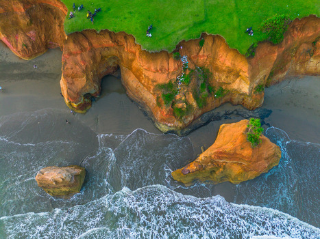 Aerial view of dramatic orange coastal cliffs with lush green grass on top and waves crashing against rock formations in Bali Bali Indonesia. Aerial view of dramatic orange coastal cliffs with lush green grass on top and waves crashing against rock formations in Bali Bali Indonesia.