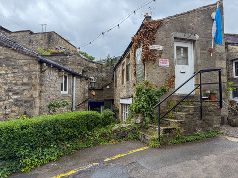 Hawes United Kingdom 06 July 2025 View of historic stone buildings in the Yorkshire Dales featuring a white door with stone steps and green hedges under a cloudy sky. Hawes United Kingdom 06 July 2025 View of historic stone buildings in the Yorkshire Dales featuring a white door with stone steps and green hedges under a cloudy sky.
