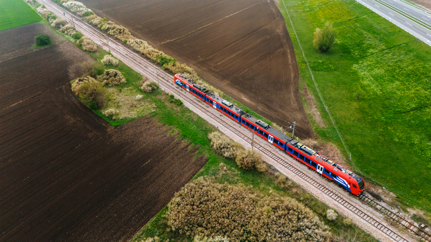 Aerial view of a red and silver train slicing through the landscape where dark soil meets vibrant green fields Sremska Mitrovica Vojvodina Serbia. Aerial view of a red and silver train slicing through the landscape where dark soil meets vibrant green fields Sremska Mitrovica Vojvodina Serbia.