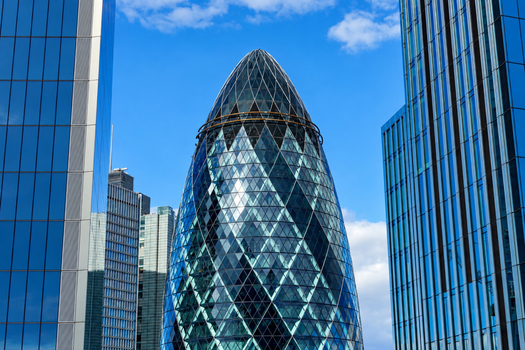 View of 30 St Mary Axe also known as The Gherkin framed by modern glass skyscrapers under a clear blue sky in London England United Kingdom. View of 30 St Mary Axe also known as The Gherkin framed by modern glass skyscrapers under a clear blue sky in London England United Kingdom.