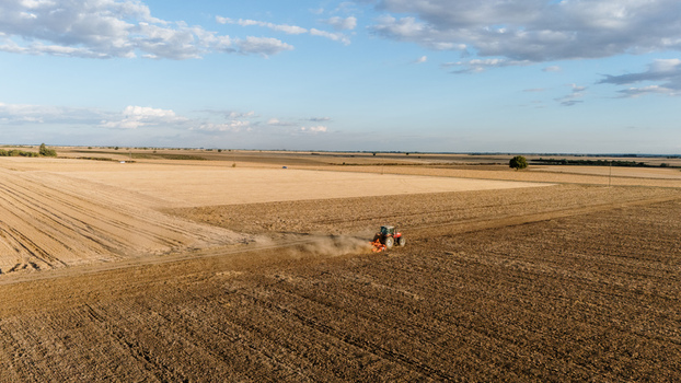 Aerial view of a red tractor plowing a vast agricultural field with dust rising in the rural landscape of Veliki Radinci Vojvodina Serbia. Aerial view of a red tractor plowing a vast agricultural field with dust rising in the rural landscape of Veliki Radinci Vojvodina Serbia.