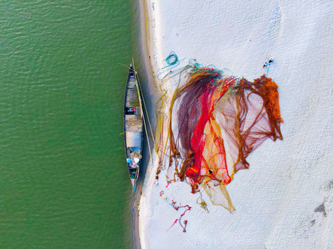 Aerial view of a traditional wooden fishing boat moored on a sandy riverbank with vibrant orange and red fishing nets spread out to dry in Kushtia Khulna Division Bangladesh. Aerial view of a traditional wooden fishing boat moored on a sandy riverbank with vibrant orange and red fishing nets spread out to dry in Kushtia Khulna Division Bangladesh.
