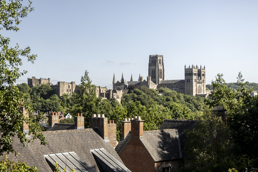View of Durham Cathedral and Durham Castle rising above the surrounding lush green trees and historic brick rooftops Durham England United Kingdom. View of Durham Cathedral and Durham Castle rising above the surrounding lush green trees and historic brick rooftops Durham England United Kingdom.
