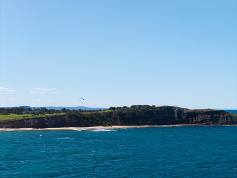 Aerial view of the Northern Beaches coastline featuring rugged cliffs sandy beach blue ocean and a paraglider in the sky in Northern Beaches Council New South Wales Australia.