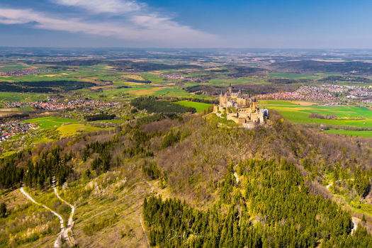 Hechingen Germany 27 September 2026 Aerial view of Hohenzollern Castle perched on a forested hilltop surrounded by rolling green fields and distant villages under a clear blue sky.