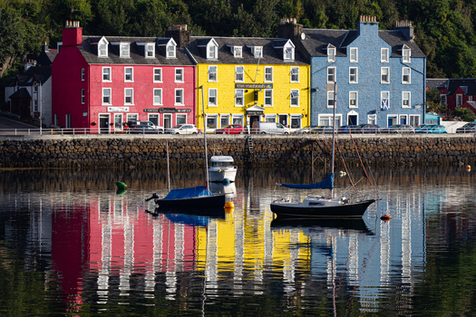 View of the iconic colorful houses along the waterfront with boats moored in the harbor and vibrant reflections on the water Tobermory Scotland United Kingdom.