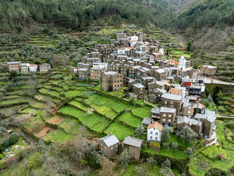 Aerial view of stone houses nestled on terraces a church spire piercing the skyline in Piódão a tapestry of green and grey Piódão Arganil Portugal. Aerial view of stone houses nestled on terraces a church spire piercing the skyline in Piódão a tapestry of green and grey Piódão Arganil Portugal.