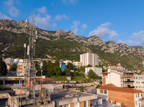 Aerial view of a telecommunications tower on a rooftop overlooking the town and rugged mountains in Kruje Durres County Albania.