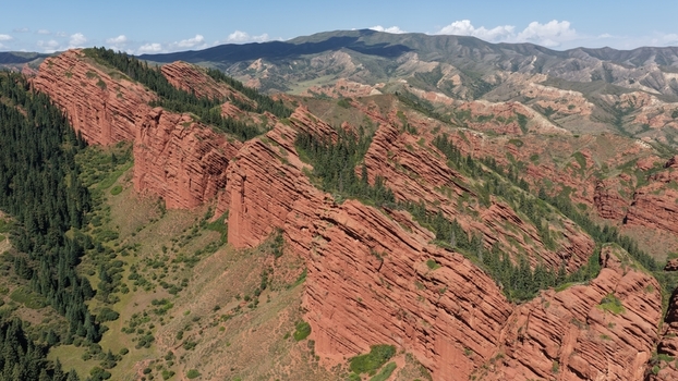 Aerial view of the red sandstone rock formations of Jety Oguz surrounded by pine forests and rugged mountain slopes under a clear blue sky in Jety Oguz Issyk Kul Region Kyrgyzstan. Aerial view of the red sandstone rock formations of Jety Oguz surrounded by pine forests and rugged mountain slopes under a clear blue sky in Jety Oguz Issyk Kul Region Kyrgyzstan.