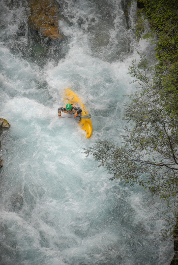 View of a kayaker in a yellow kayak navigating the white water rapids of the Rio Manso surrounded by lush green foliage in San Carlos de Bariloche Rio Negro Argentina. View of a kayaker in a yellow kayak navigating the white water rapids of the Rio Manso surrounded by lush green foliage in San Carlos de Bariloche Rio Negro Argentina.