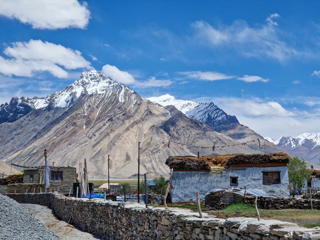 View of Penzi La road with traditional white washed houses stone walls and prayer flags set against the backdrop of the snow capped Himalayan mountains in Zanskar Ladakh India.