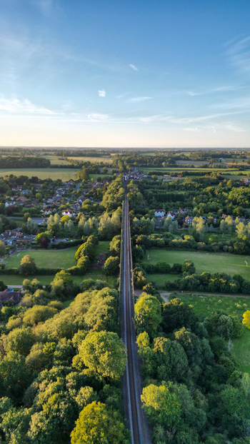 Aerial view of Chappel Viaduct stretching through the lush green countryside of Essex with trees and rural landscape under a clear blue sky in Chappel England United Kingdom.