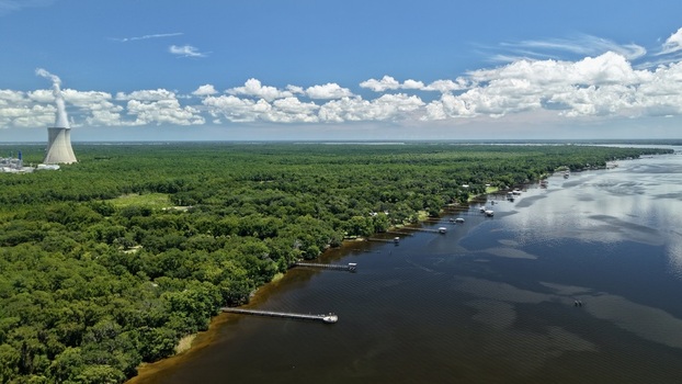 Aerial view of the Seminole Electric Cooperative power plant cooling tower emitting steam surrounded by forest and wooden piers along the St. Johns River Palatka Florida United States.