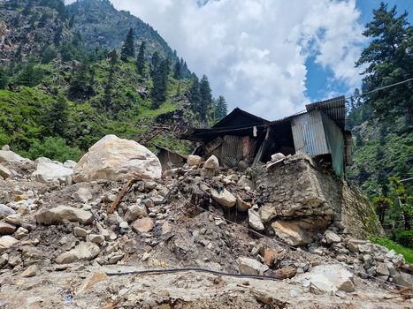 View of a damaged house surrounded by large boulders and debris from a landslide in the mountainous terrain of Malana Himachal Pradesh India.