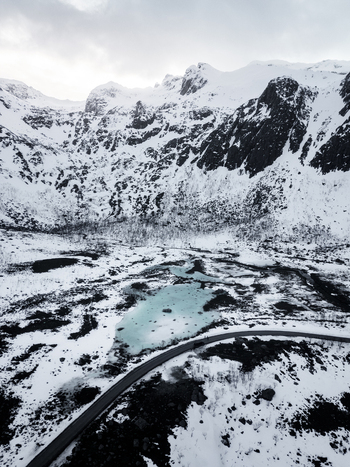 Aerial view of Grotfjord featuring a turquoise lake and a winding road amidst snow covered peaks in Tromvik Troms Norway. Aerial view of Grotfjord featuring a turquoise lake and a winding road amidst snow covered peaks in Tromvik Troms Norway.