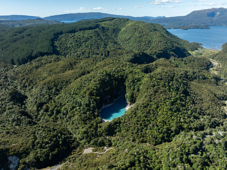 Aerial view of the vivid turquoise lake nestled within the verdant embrace of dense forest a serene contrast against the distant blue waters Waimangu New Zealand. Aerial view of the vivid turquoise lake nestled within the verdant embrace of dense forest a serene contrast against the distant blue waters Waimangu New Zealand.