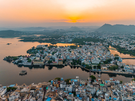 Aerial view of the historic city of Udaipur situated along the shores of Lake Pichola at sunset with golden light reflecting on the water and surrounding hills in Udaipur Rajasthan India.