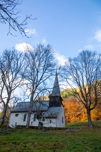 View of St. Oswald s Chapel surrounded by bare trees and vibrant autumn forest under a clear blue sky in Breitnau Baden Wurttemberg Germany. View of St. Oswald s Chapel surrounded by bare trees and vibrant autumn forest under a clear blue sky in Breitnau Baden Wurttemberg Germany.
