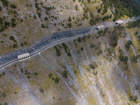 Aerial view of the Albanian Alps mountain road with tunnels carved into the rocky cliffside surrounded by steep slopes and sparse vegetation in Shkoder Shkoder County Albania. Aerial view of the Albanian Alps mountain road with tunnels carved into the rocky cliffside surrounded by steep slopes and sparse vegetation in Shkoder Shkoder County Albania.