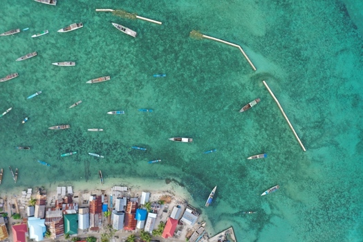 Aerial view of Pulau Maginti showing a coastal village with colorful houses and small wooden boats anchored in the clear turquoise shallow water of Maginti South East Sulawesi Indonesia.