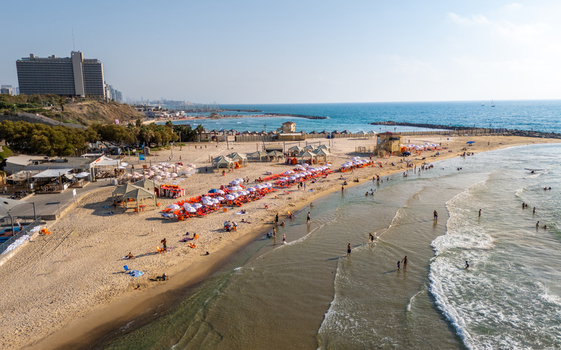Aerial view of a sandy beach with rows of orange and white umbrellas people relaxing in the Mediterranean Sea and the urban skyline of Tel Aviv Yafo Tel Aviv District Israel. Aerial view of a sandy beach with rows of orange and white umbrellas people relaxing in the Mediterranean Sea and the urban skyline of Tel Aviv Yafo Tel Aviv District Israel.