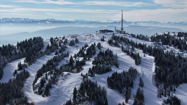 Aerial view of the snow laden slopes of Mont Saint Michel contrasted against the distant hazy mountains Gex Auvergne Rhône Alpes France. Aerial view of the snow laden slopes of Mont Saint Michel contrasted against the distant hazy mountains Gex Auvergne Rhône Alpes France.