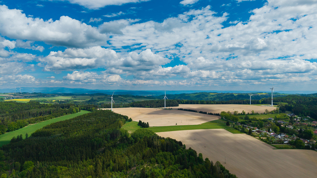 Aerial view of wind turbines standing in open fields surrounded by dense green forests under a blue sky with white clouds near Zipotin Gruna Pardubicky kraj Czechia. Aerial view of wind turbines standing in open fields surrounded by dense green forests under a blue sky with white clouds near Zipotin Gruna Pardubicky kraj Czechia.