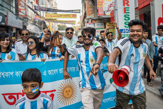 Bogura Bangladesh 02 December 2022 View of fans wearing Argentina national football team jerseys celebrating in the street with a banner and a megaphone.