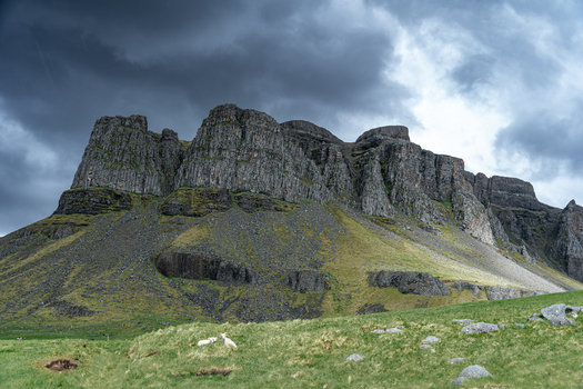 View of the rugged cliffs of Hvalfjordur under dark storm clouds with green grassy slopes and sheep in the foreground Iceland. View of the rugged cliffs of Hvalfjordur under dark storm clouds with green grassy slopes and sheep in the foreground Iceland.