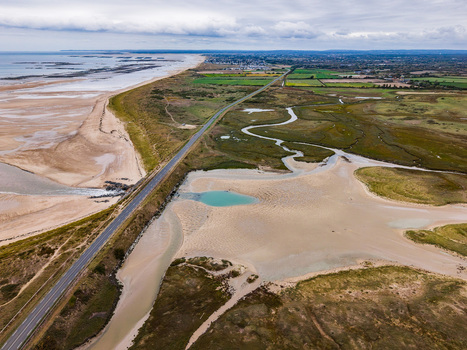 Aerial view of the Havre de Geffosses featuring winding tidal channels expansive sand flats and a coastal road bordering green fields in Geffosses Normandy France.