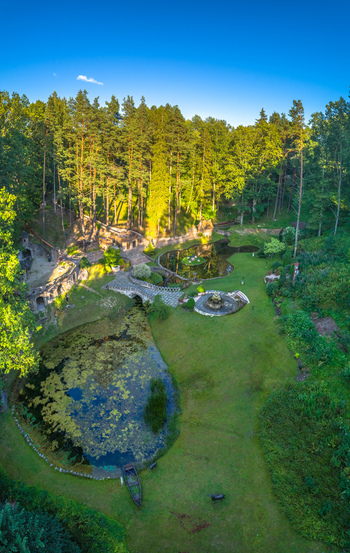 Aerial view of a lush park featuring ponds a stone bridge and a fountain surrounded by dense forest trees in Latvia. Aerial view of a lush park featuring ponds a stone bridge and a fountain surrounded by dense forest trees in Latvia.