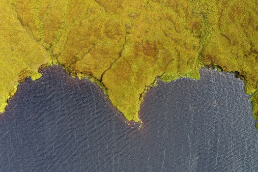 Aerial view of the rugged coastline with vibrant green grassy terrain meeting the dark waters of the lake in Portree Scotland United Kingdom. Aerial view of the rugged coastline with vibrant green grassy terrain meeting the dark waters of the lake in Portree Scotland United Kingdom.