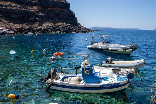 View of small boats and dinghies floating on clear turquoise water near the rocky volcanic cliffs of Santorini in Fira Greece. View of small boats and dinghies floating on clear turquoise water near the rocky volcanic cliffs of Santorini in Fira Greece.
