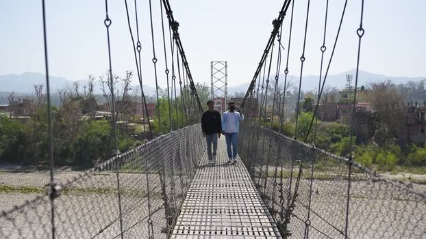 View of two men walking on a suspension bridge Nepal.