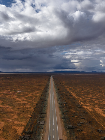 Aerial view of a long straight road stretching through the arid outback landscape under a dramatic storm cloud sky in Flinders Ranges South Australia Australia.