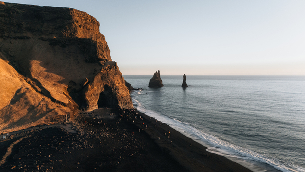 Aerial view of basalt sea stacks rise majestically from the turbulent Atlantic contrasting sharply with the black sands of Reynisfjara beach Reynisdrangar Iceland.