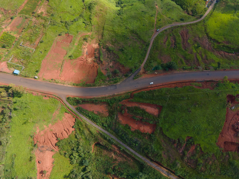 Aerial view of the Kaas plateau landscape featuring winding roads lush green vegetation and patches of exposed reddish soil in Satara Maharashtra India.