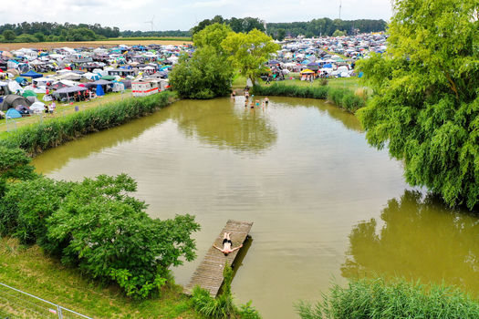 Herzogenaurach Germany 26 July 2025 Aerial view of the Open Beatz Festival featuring a pond with people swimming and a person on a pier next to a large campsite with tents.