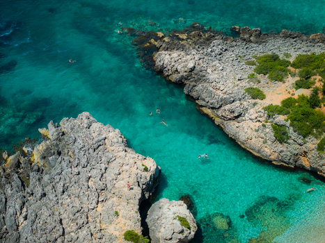 Aerial view of Aquarium Beach featuring turquoise waters and rocky cliffs with people swimming in the crystal clear sea Jala Vlore County Albania. Aerial view of Aquarium Beach featuring turquoise waters and rocky cliffs with people swimming in the crystal clear sea Jala Vlore County Albania.