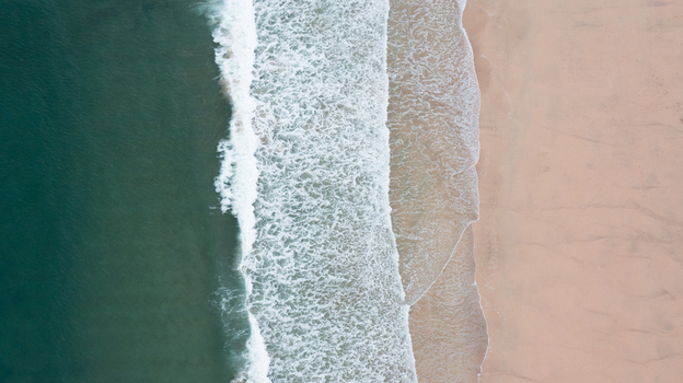 Aerial view of turquoise ocean waves crashing on the golden sand of Harlyn Bay Beach in Saint Merryn Cornwall United Kingdom.